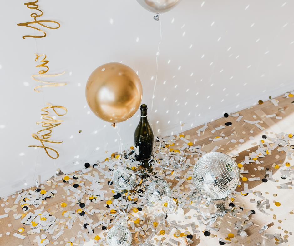 champagne bottle on the ground surrounded by confetti and balloons for new years eve